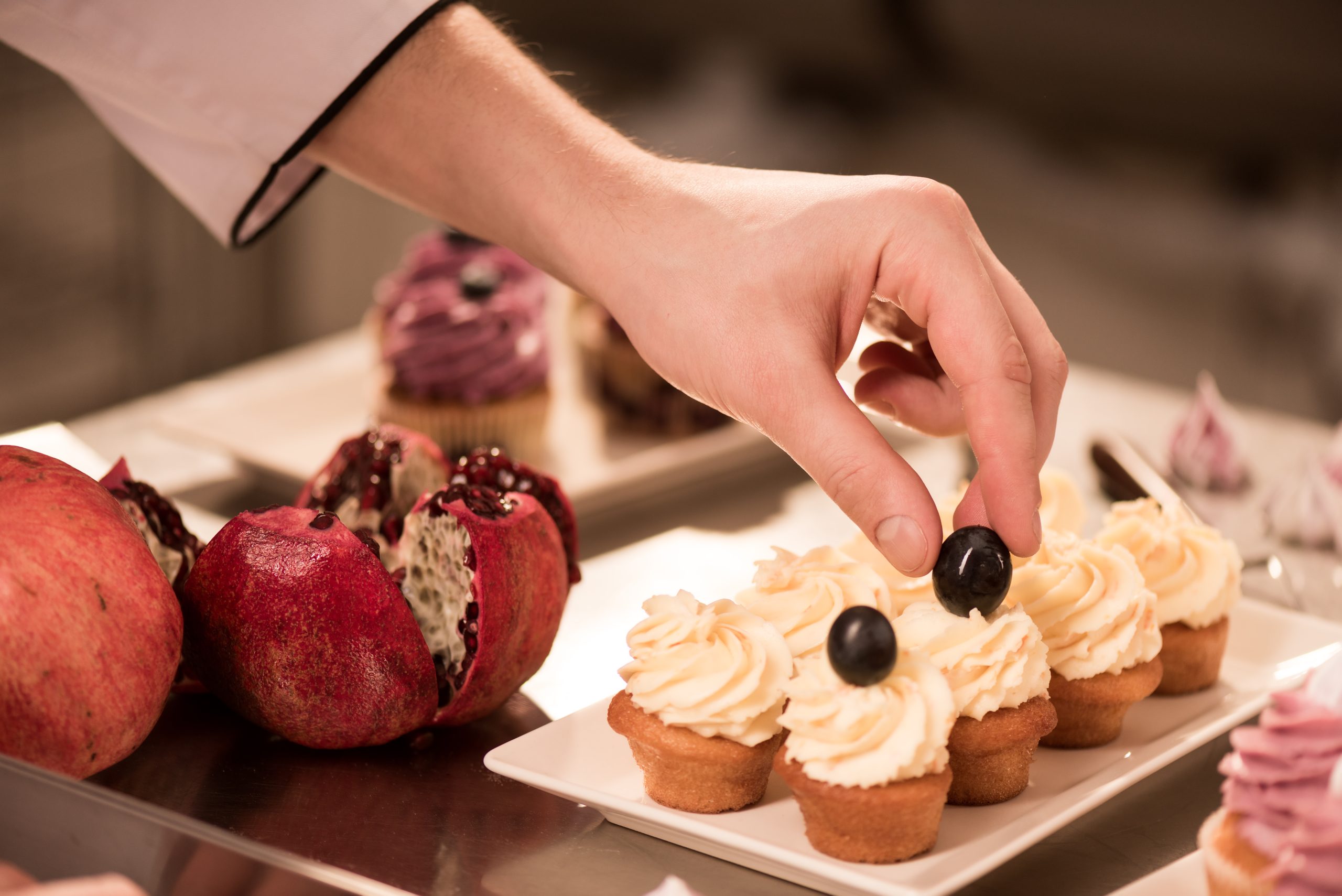 cropped shot of confectioner decorating sweet cupcakes