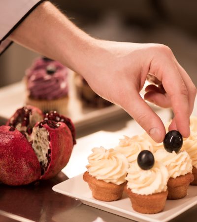 cropped shot of confectioner decorating sweet cupcakes